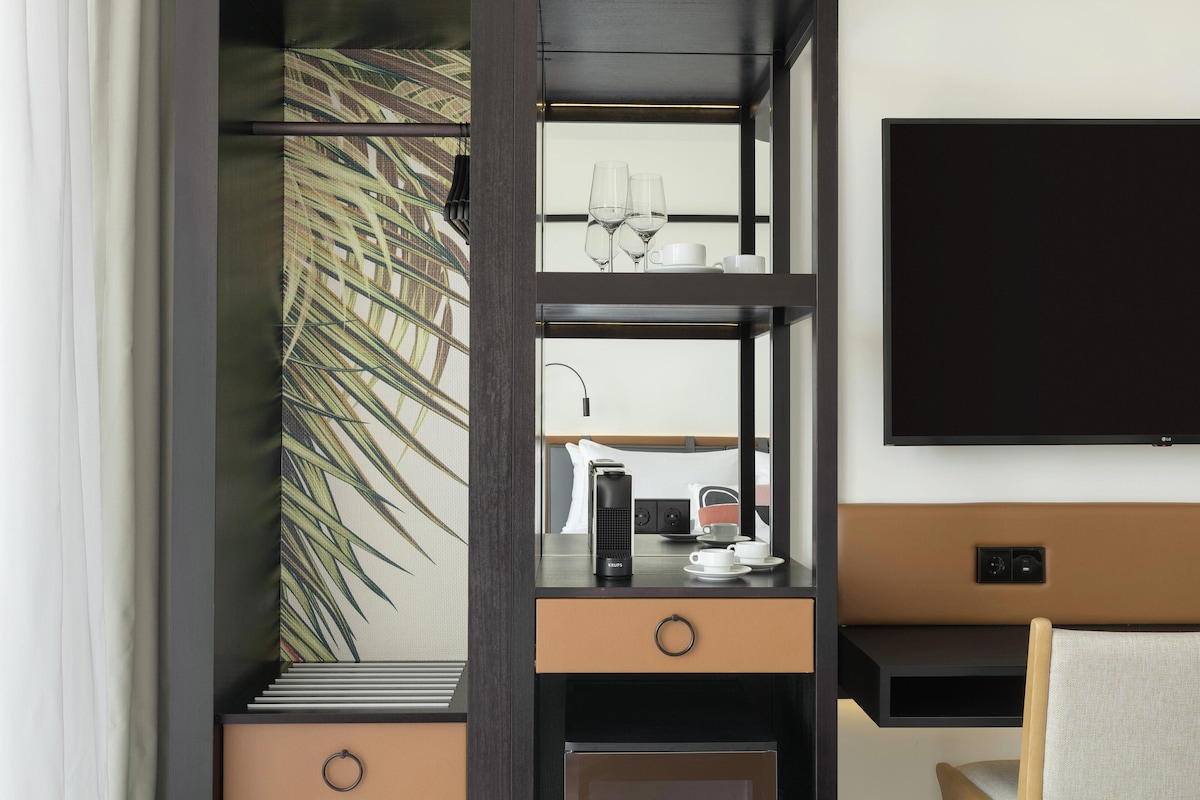 Une chambre d’hôtel moderne dotée d’un bureau intégré, d’un téléviseur à écran plat, d’une machine à café et d’une plante décorative.