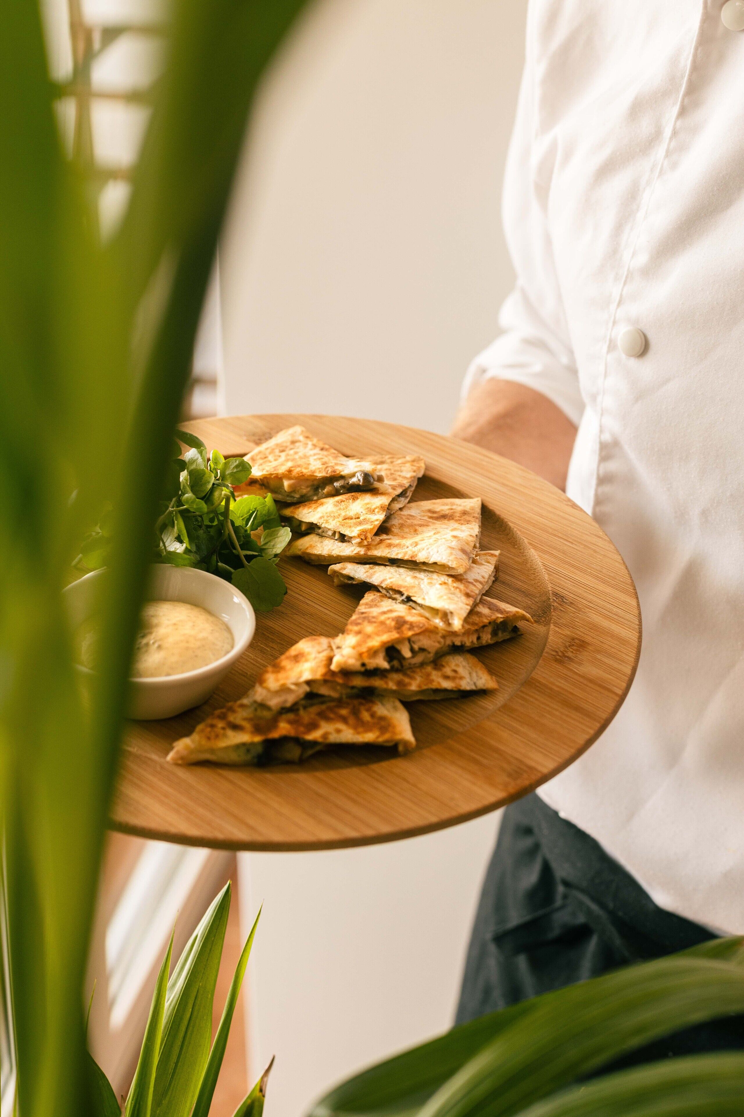 Uma pessoa segurando uma tábua de madeira com quesadillas e uma pequena tigela de molho.