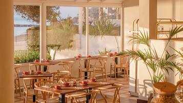 An indoor dining area with wooden tables and chairs, large windows with a view of the outdoors, and various jars and containers on the tables.
