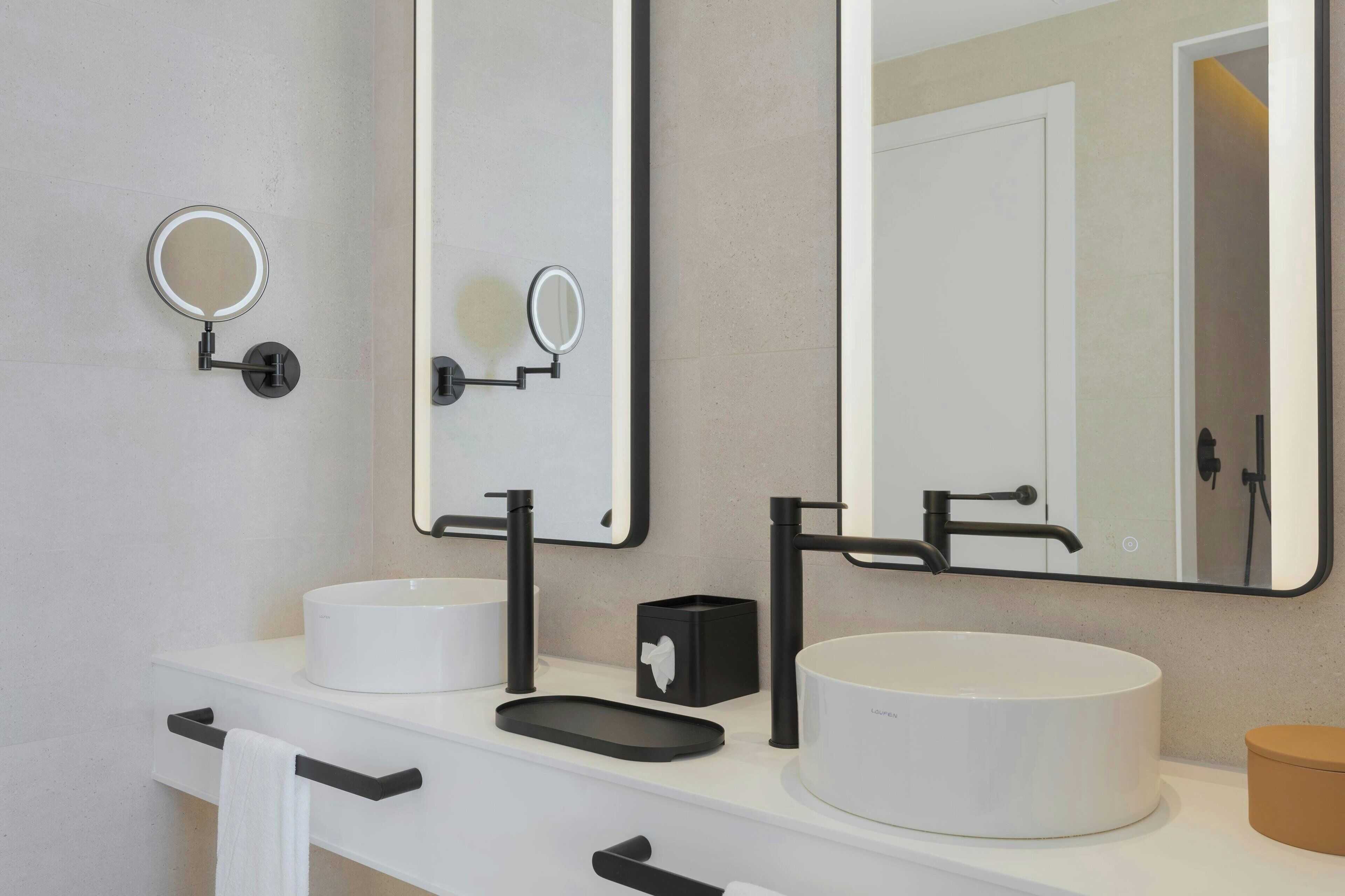 A bathroom with two round white sinks, a large mirror, and a towel rack.