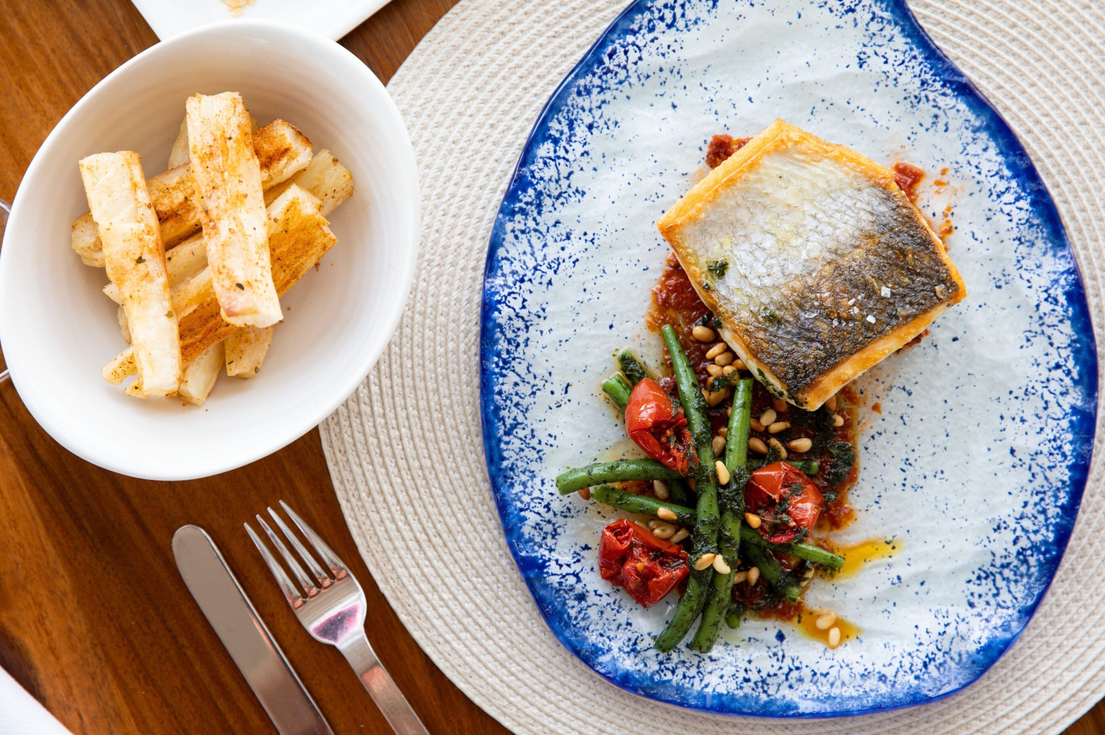 Un plato con pescado, judías verdes, tomates y un bol de papas fritas.