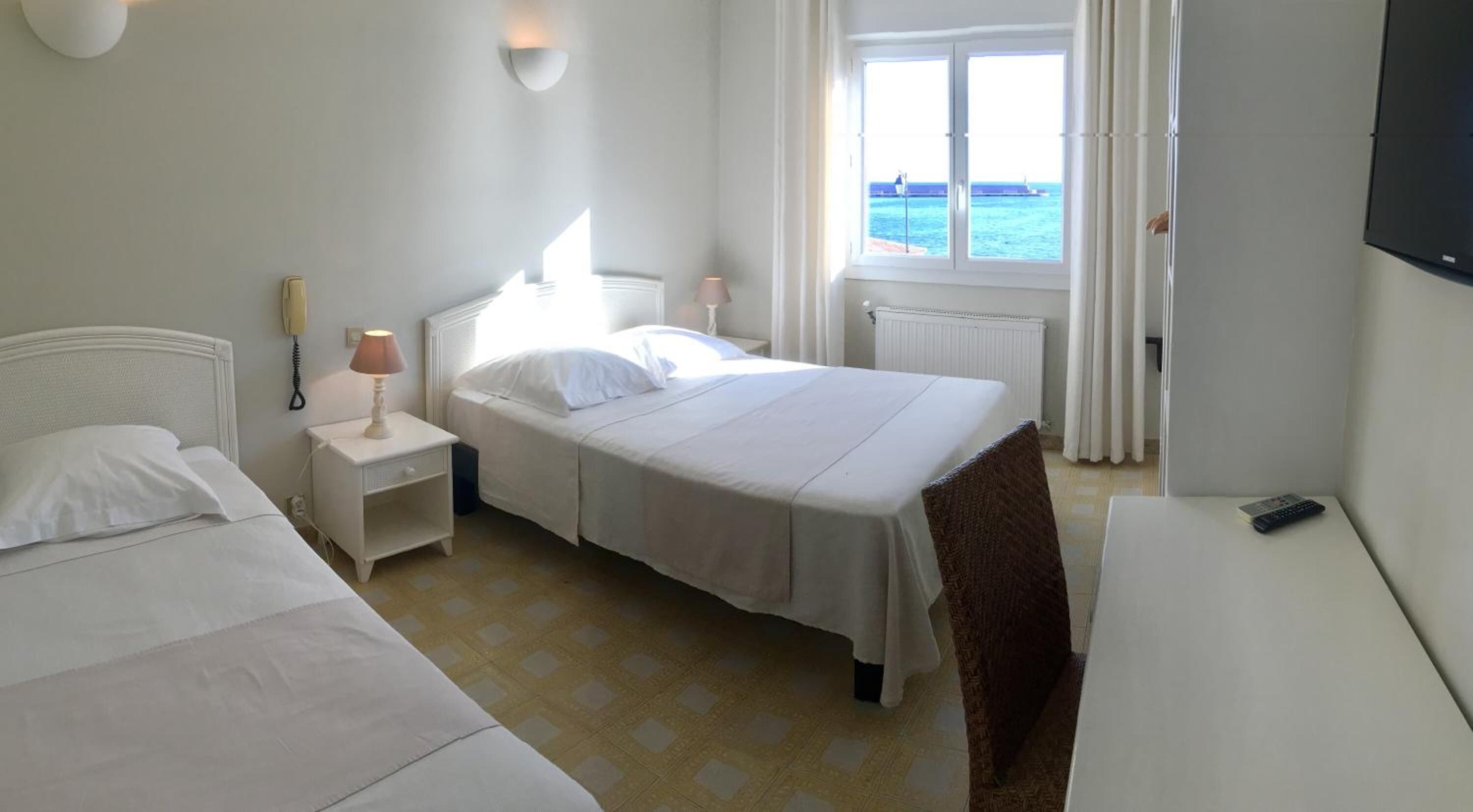 A hotel room with a bed, bedside table, lamp, and a view of the sea through the window.