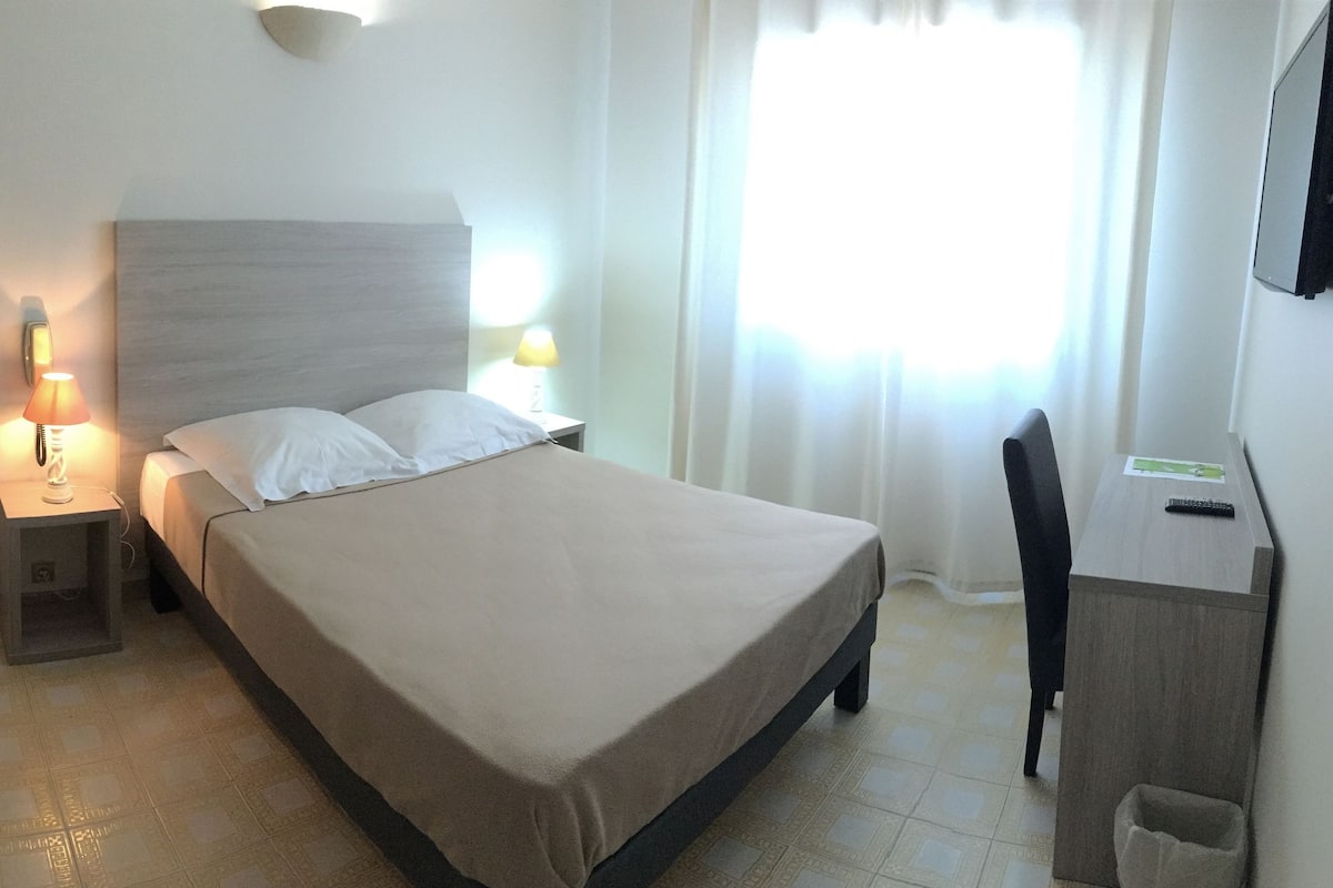 A hotel room with a bed, bedside lamps, a chair, a desk, and a TV.