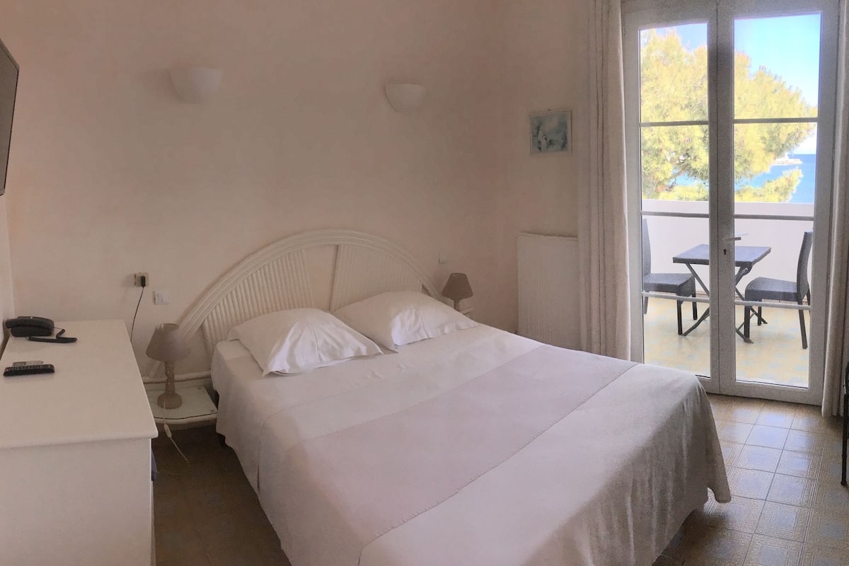A bedroom with a bed, a desk, a chair, and a view of an outdoor patio with a table and chairs.