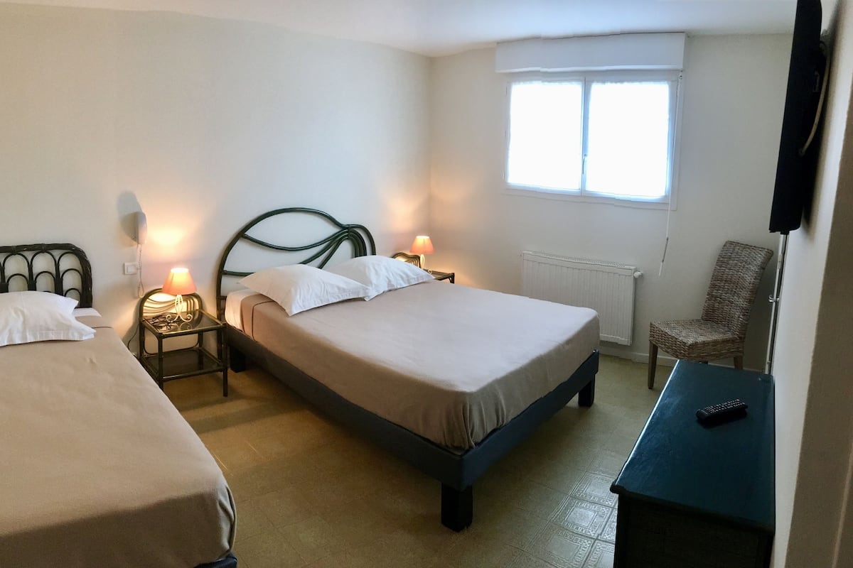 A hotel room with two single beds, a chair, a small table, and a window.