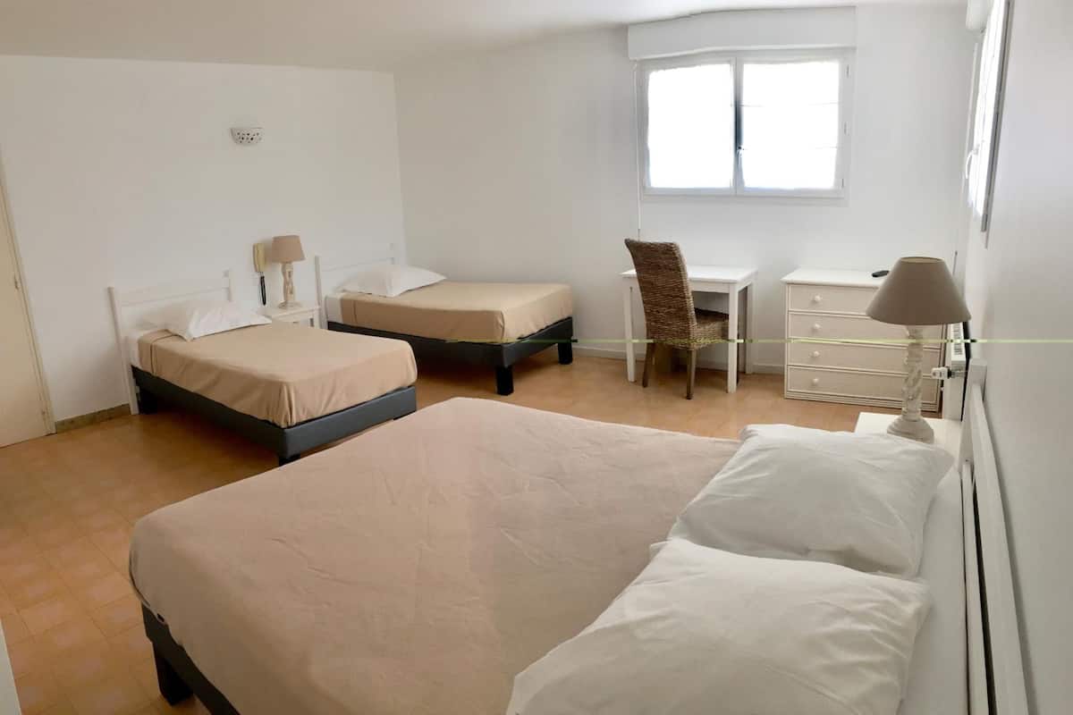 A hotel room with two single beds, a desk, a chair, and a window.