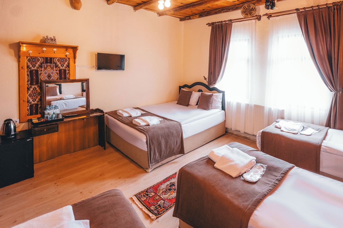 Habitación de hotel con techo de madera, una cama con cabecera, un pequeño escritorio con espejo, televisor y una zona de estar con banco.