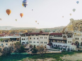 Un edificio histórico con varios balcones y ventanas arqueadas, rodeado de vegetación y un paisaje rocoso.