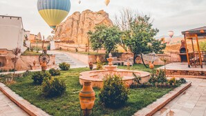 A courtyard with a fountain, outdoor seating, and a view of hot air balloons in the distance. - TURBEL CAVE HOUSE (Avanos)
