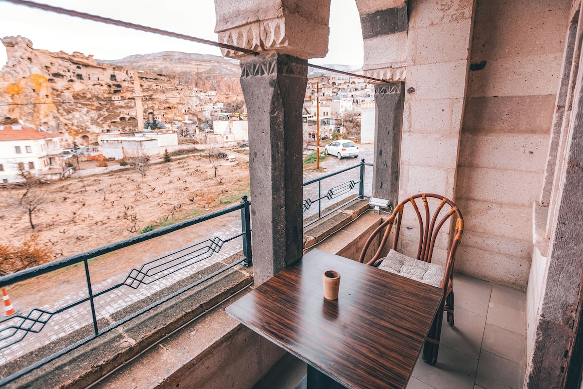 Un balcón con mesa y sillas, con vistas a un pueblo montañoso con edificios y cielo despejado.