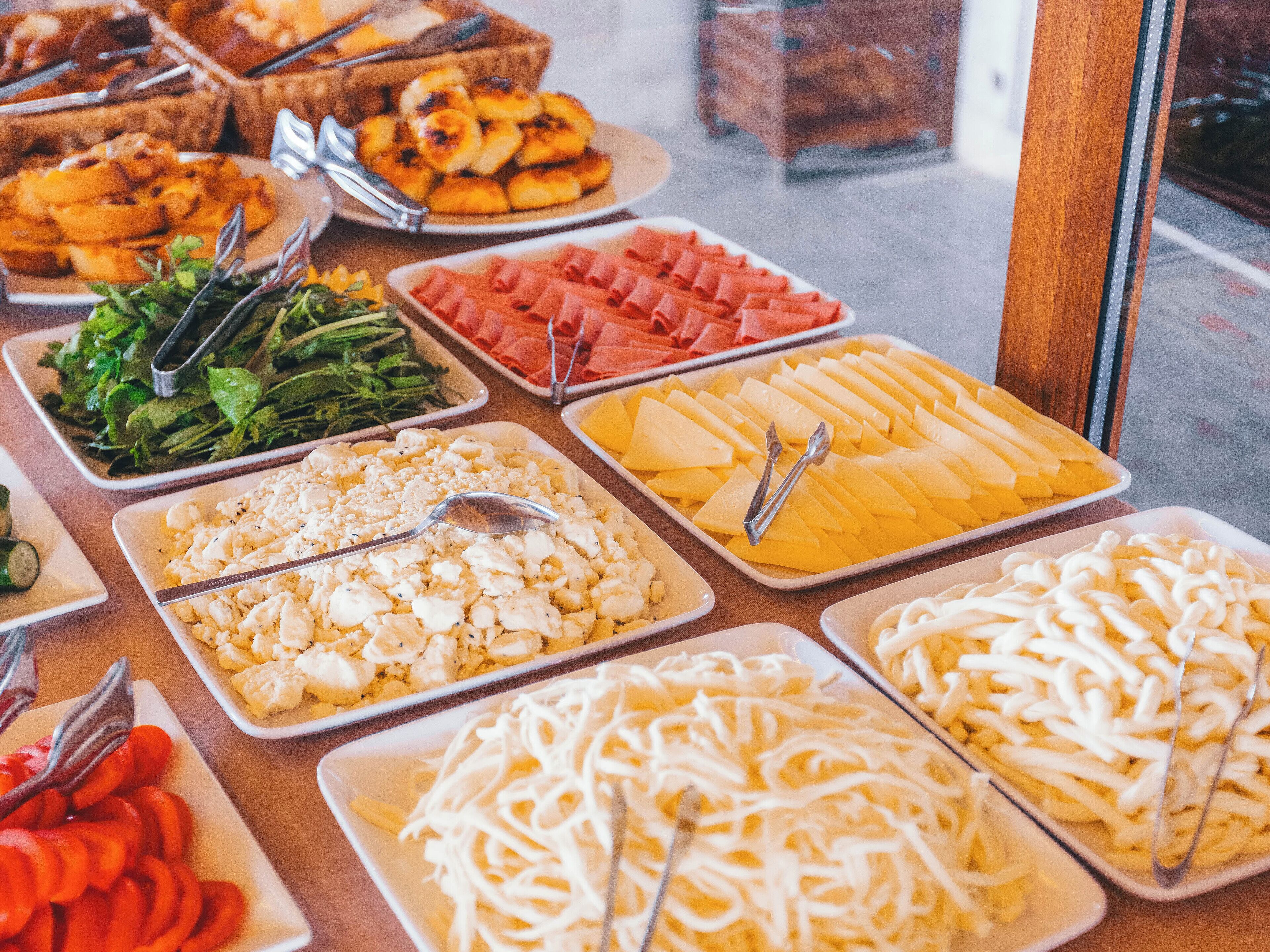 Un bufé con diferentes opciones de comida, incluyendo ensaladas, quesos y carnes.