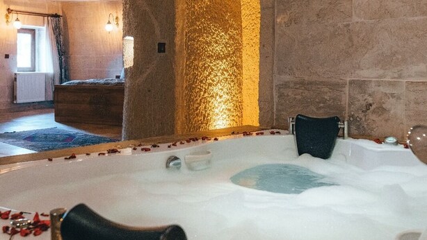 Un cuarto de spa con una bañera grande llena de agua, rodeada de pétalos de rosa.