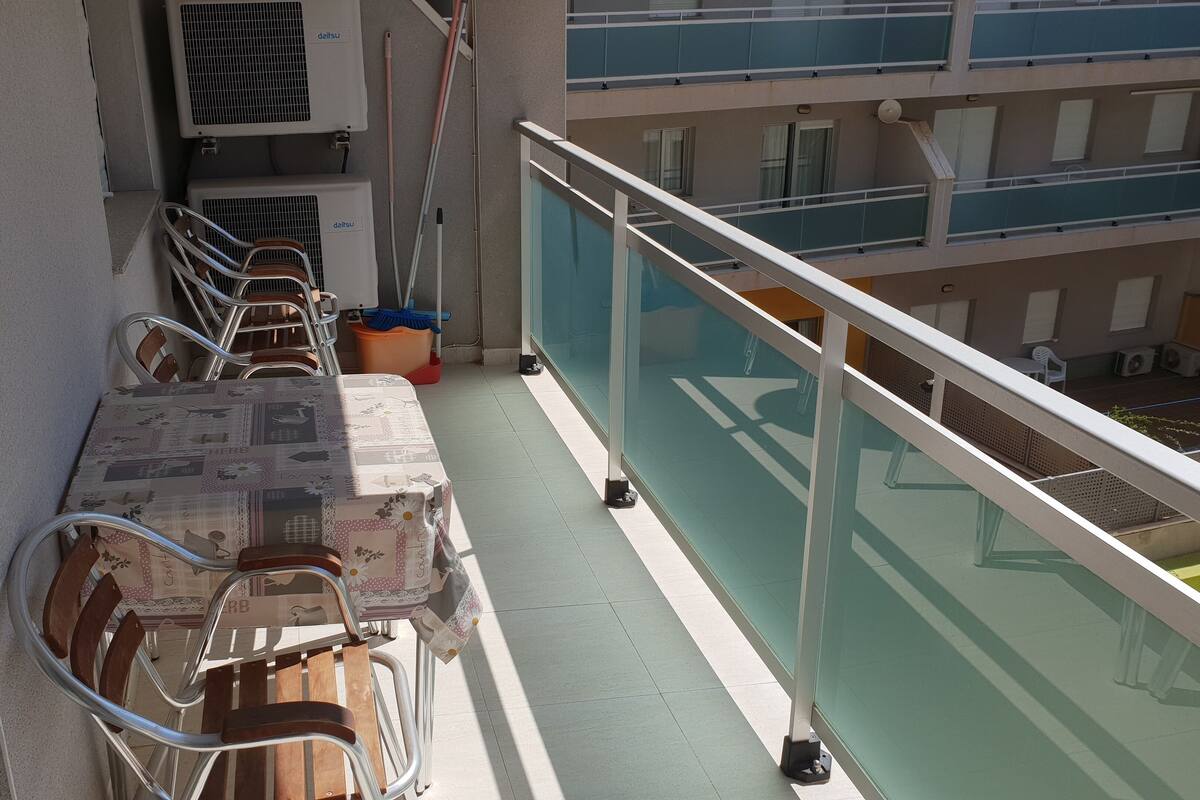A balcony with a table set for dining, chairs, a mop, and a bucket.