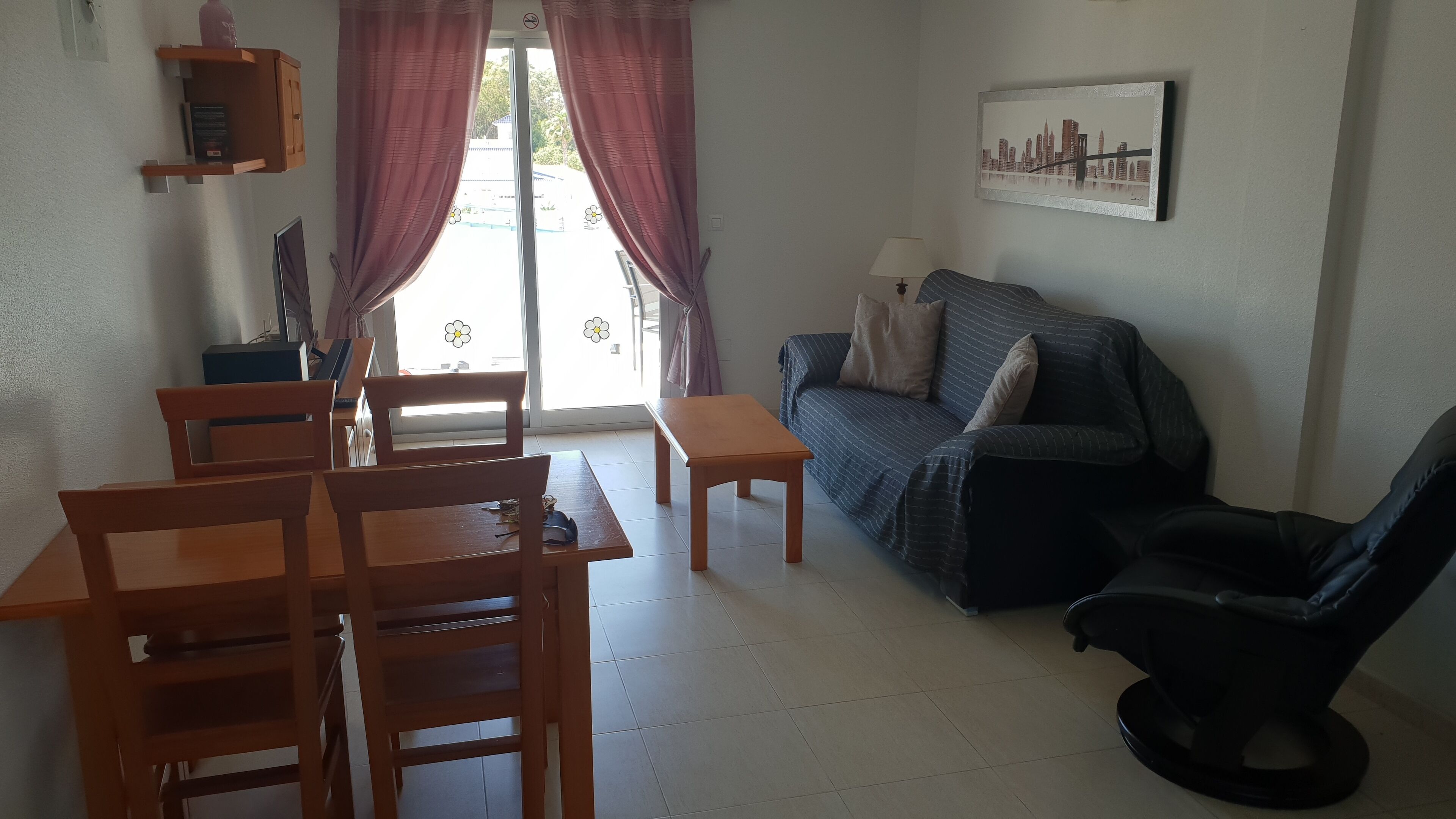 Una sala de estar con un sofá, una mesa de comedor con sillas, una pequeña mesa de madera y una silla negra.