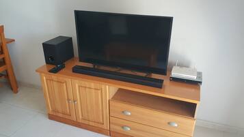 A wooden entertainment center with a flat-screen TV, a soundbar, a remote control, and a router.