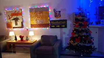 A living room with a Christmas tree, two lamps, and a sign for Manhattan Quality HomeFood Restaurant.