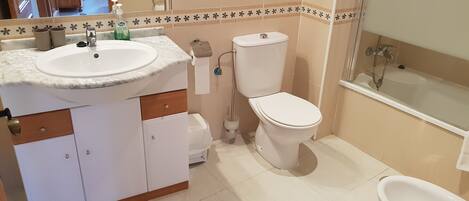 A bathroom with a white sink, toilet, and bidet. There is a mirror above the sink, and the walls are tiled with a floral pattern.