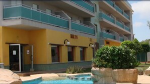 Un hotel a più piani con balconi, piscina e un giardino curato.