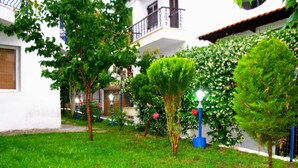 A courtyard with a well-maintained lawn, several trees, and a blue lamp post. - Anemos Hotel (Kassandra)