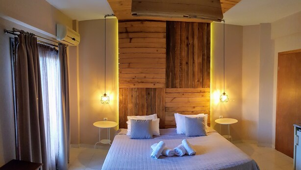 A bedroom with a large bed, two bedside tables, a wooden headboard, and two wall-mounted lamps. - Anemos Hotel (Kassandra)