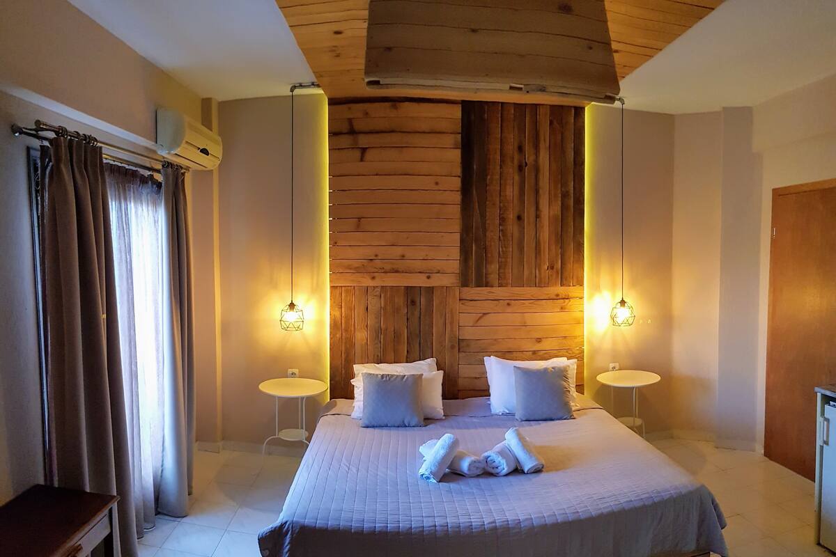 A bedroom with a large bed, two bedside tables, a wooden headboard, and two wall-mounted lamps.