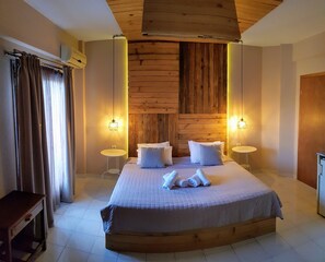 A bedroom with a large bed, two bedside tables, a wooden headboard, and two wall-mounted lamps. - Anemos Hotel (Kassandra)