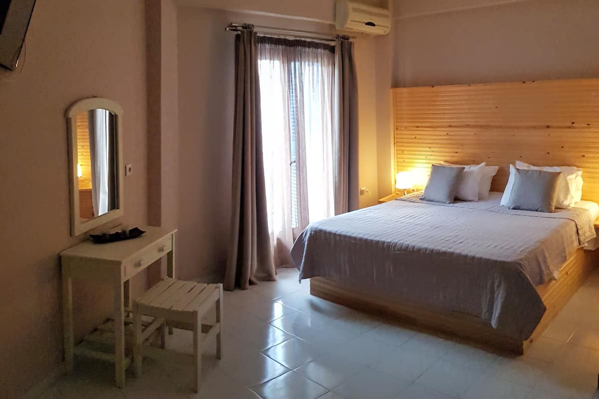 A hotel room with a large bed, a desk with a chair, a mirror, and a window with curtains.