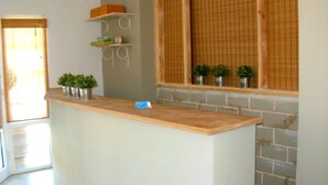 A kitchen with a wooden countertop, a brick wall, and a window with bamboo blinds. - Anemos Hotel (Kassandra)