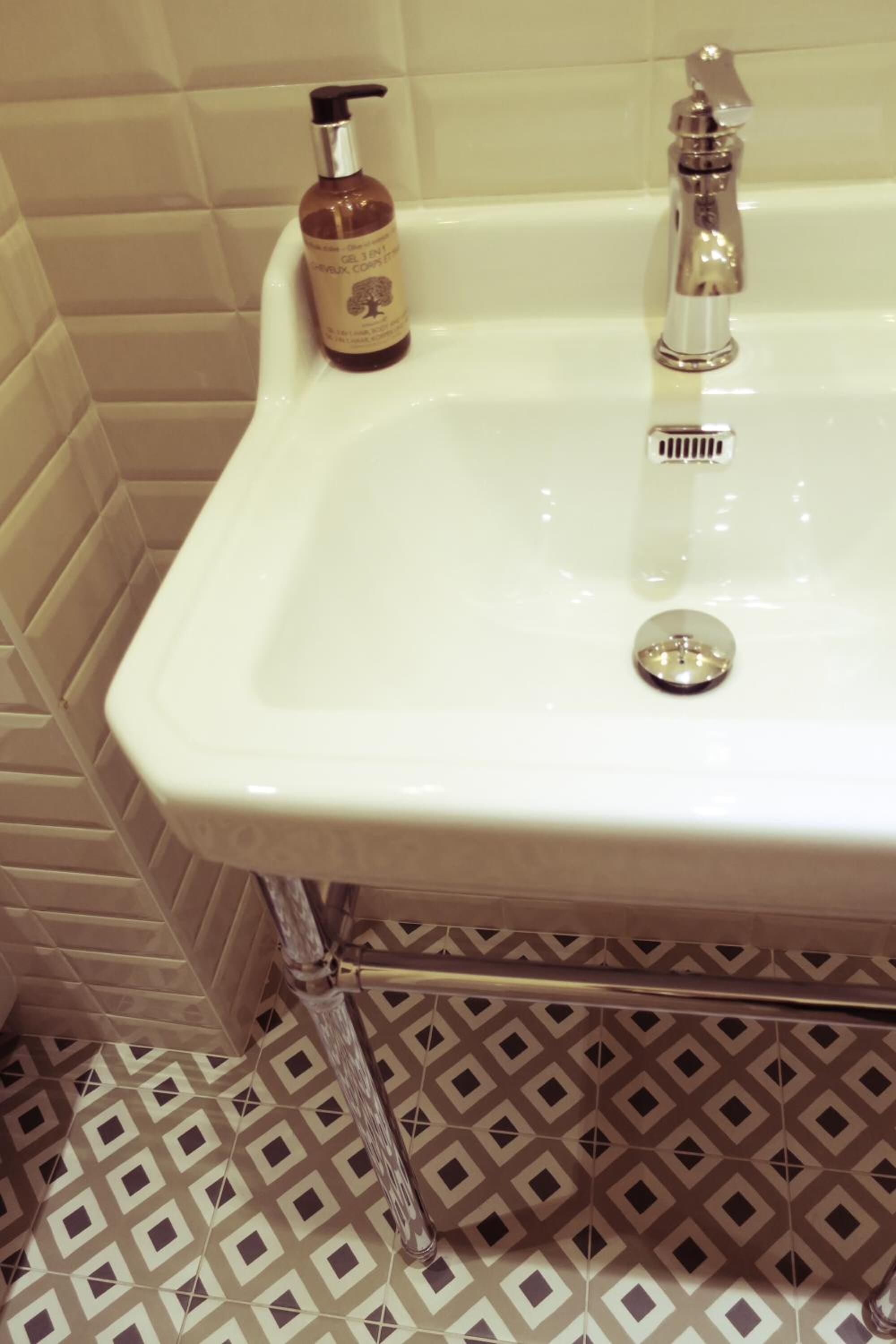 Un baño con un lavabo blanco, una botella de champú y un grifo.