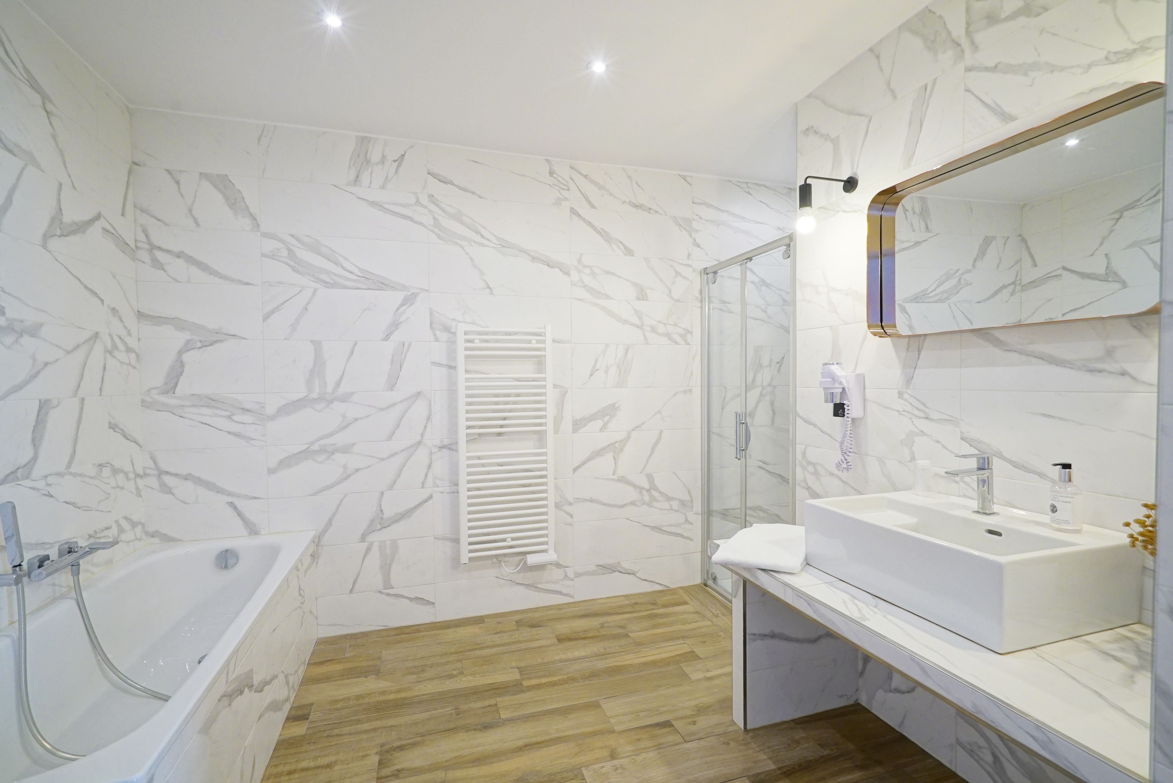 A modern bathroom with a marble wall, a bathtub, a glass shower enclosure, and a vanity with a sink and mirror.