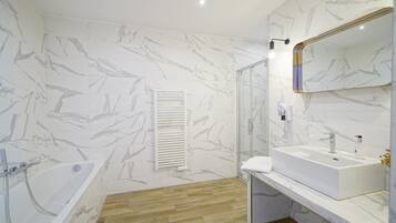 A modern bathroom with a marble wall, a bathtub, a glass shower enclosure, and a vanity with a sink and mirror.