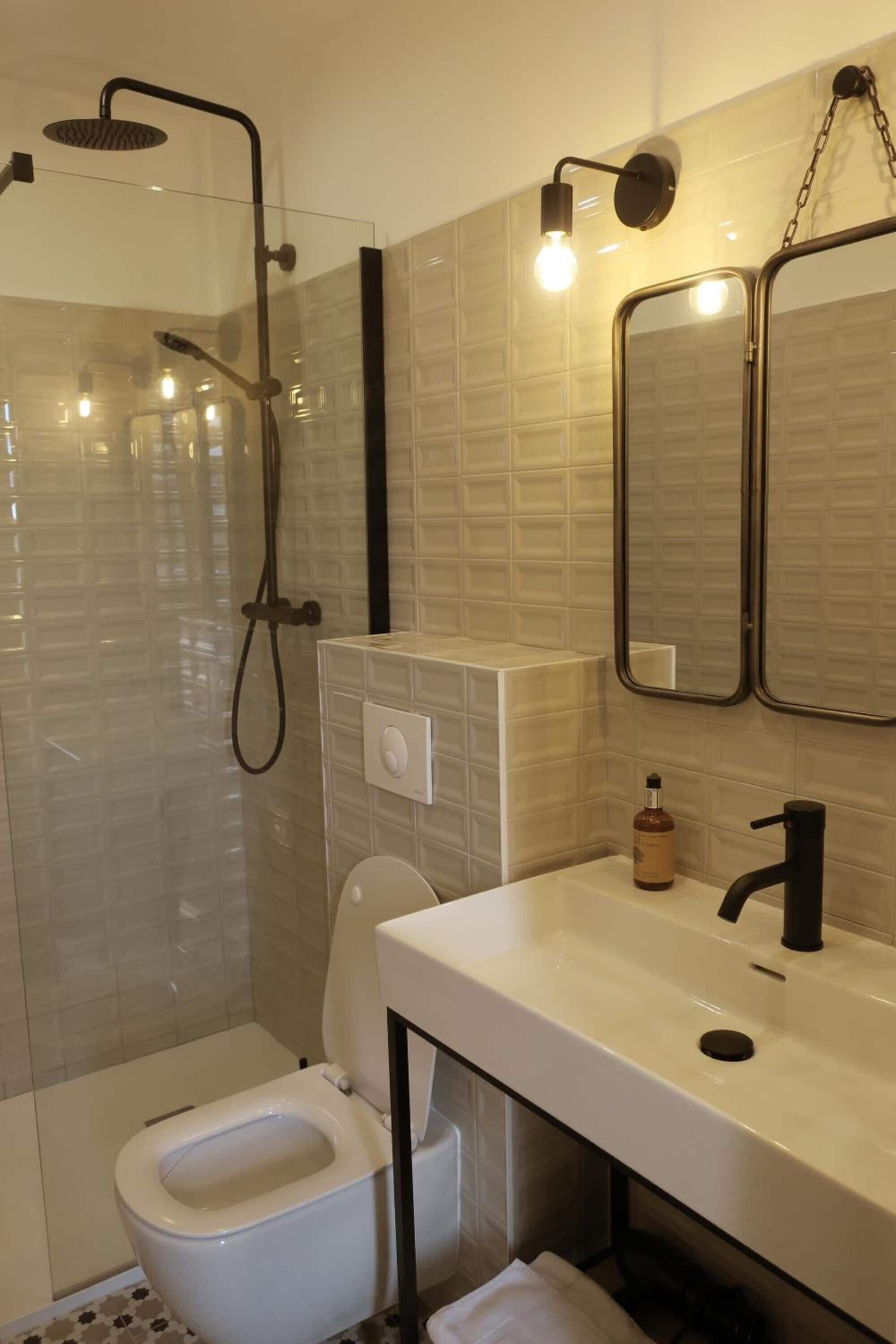 A modern bathroom with a glass-enclosed shower, a white toilet, a sink with a black faucet, and a mirror with lights.