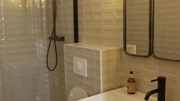 A modern bathroom with a glass-enclosed shower, a white toilet, a sink with a black faucet, and a mirror with lights.