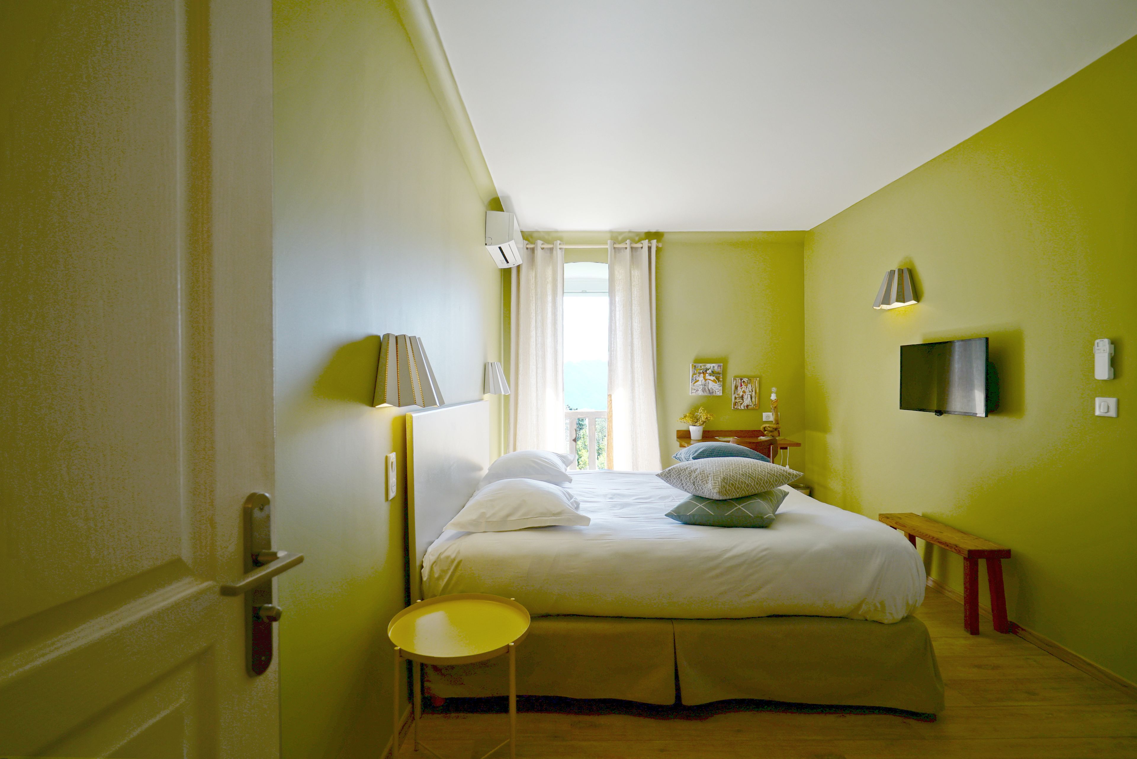 Une chambre à coucher avec un lit, une table de chevet, une lampe et un petit tabouret.