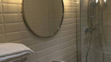 Un baño con lavamanos blanco, un espejo redondo y cabina de ducha con paredes de cristal.