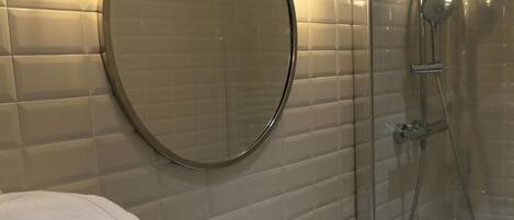 A bathroom with a white sink, a round mirror, and a glass-enclosed shower.