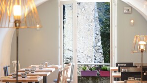 En restaurant med dækkede borde, et stort vindue med udsigt til et klippefyldt landskab og indretningsbelysning.