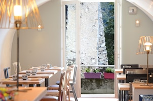 Restaurante com mesas postas para refeições, uma grande janela com vista para uma paisagem rochosa e luminárias.