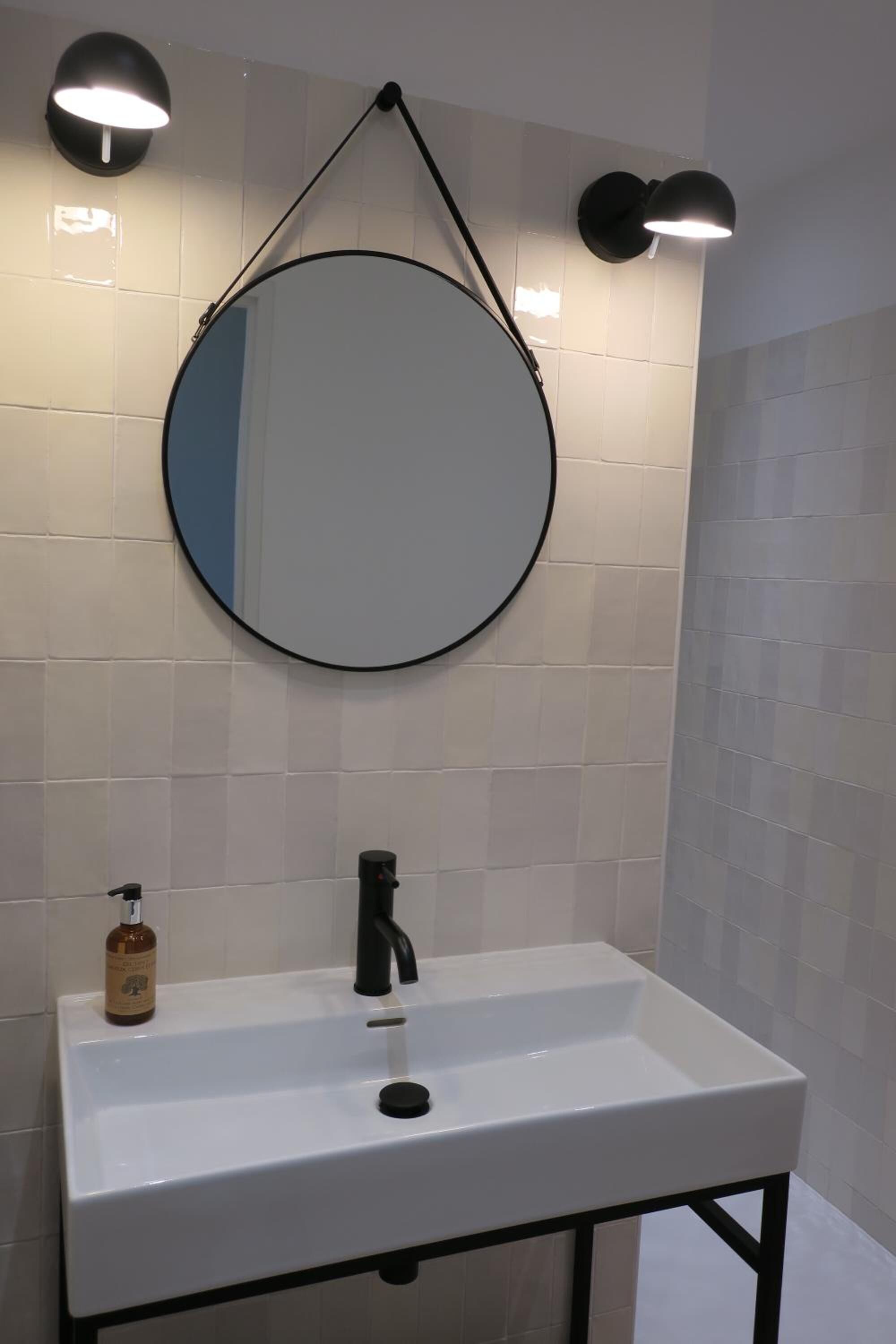 Un baño con lavamanos blanco, un espejo redondo y dos luces fijadas a la pared.