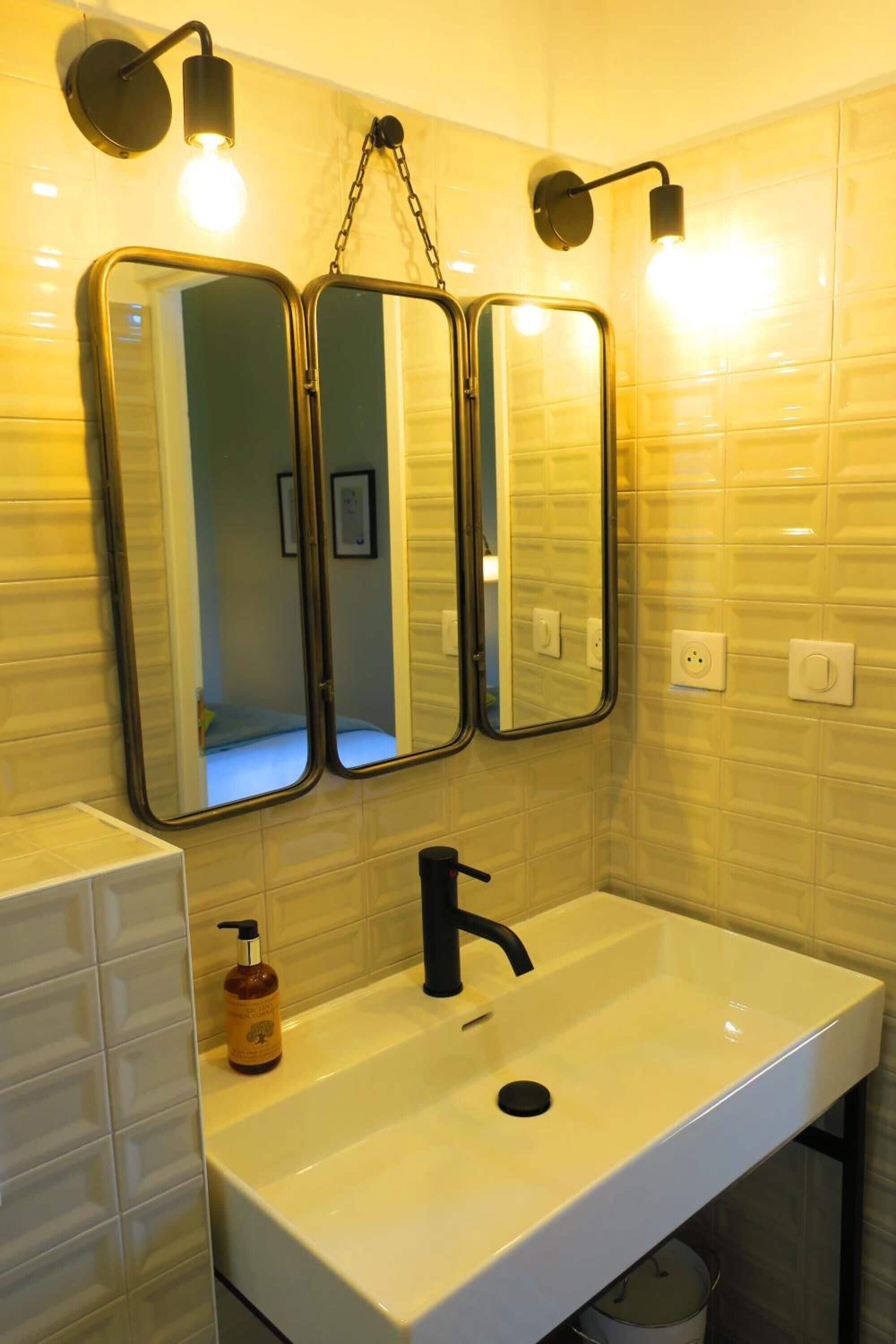 A bathroom with a white sink, a black faucet, and three mirrors mounted on the wall.