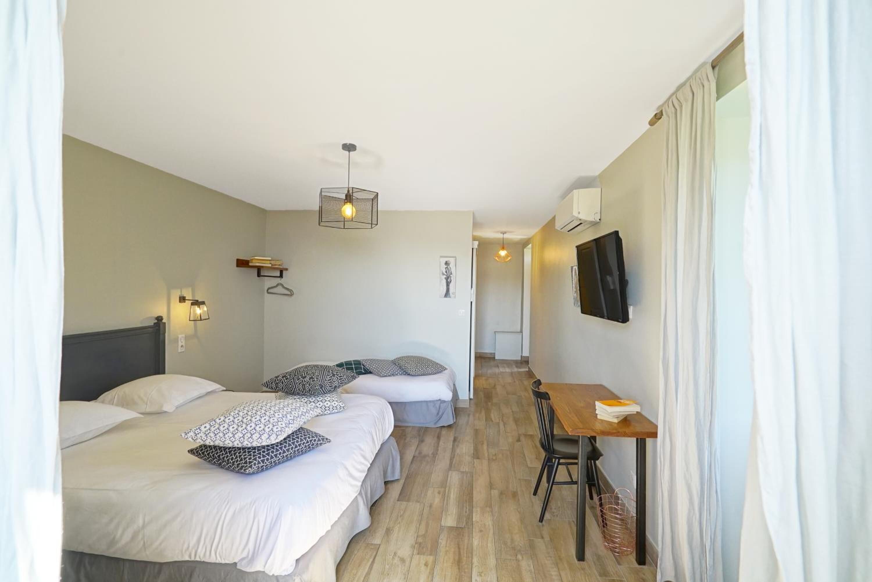 A hotel room with two beds, a desk, a chair, a TV, and a hanging light fixture.