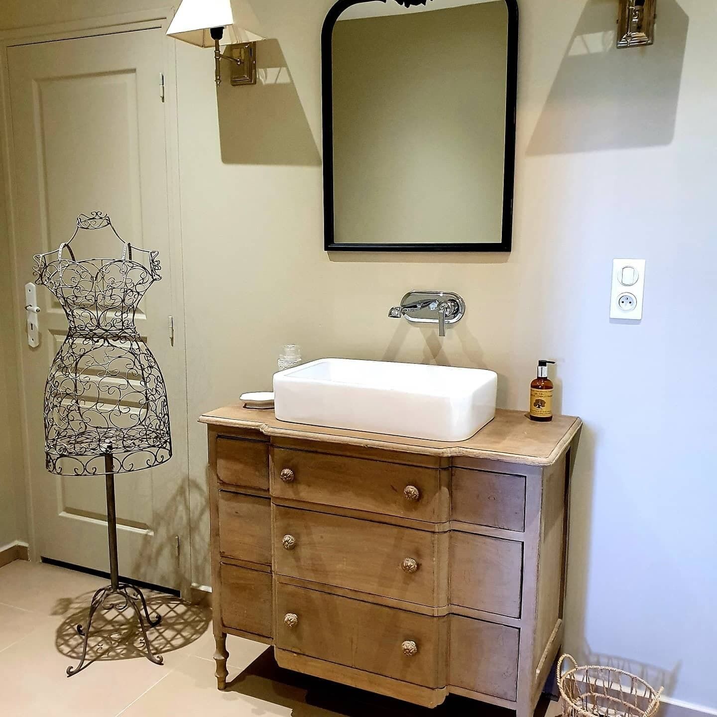 Un baño con tocador de madera, un espejo y una lámpara de metal.