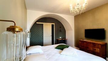 A bedroom with a large bed, a chandelier, a television, and a wooden dresser.