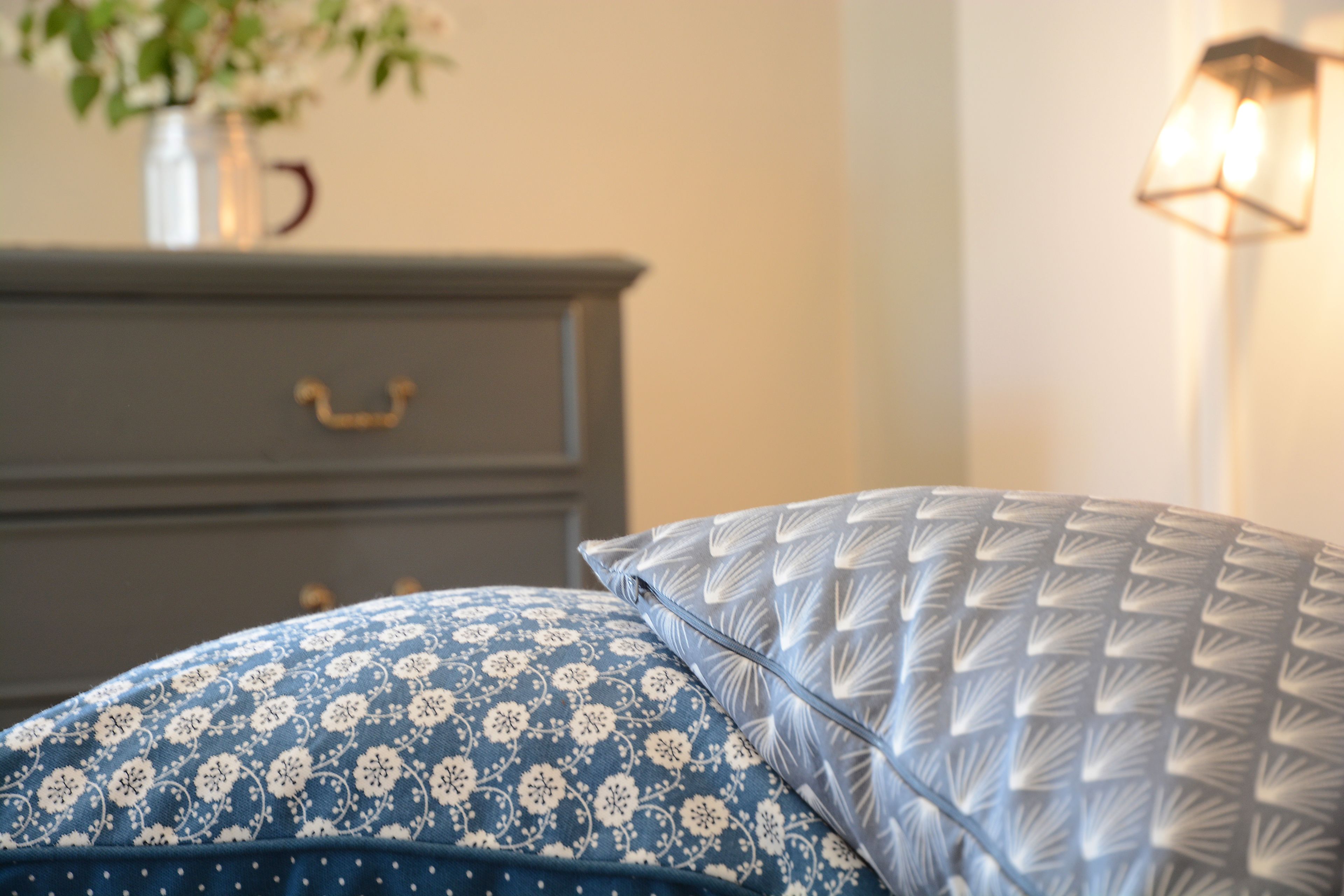 A bed with patterned pillows, a dresser, and a vase with flowers.