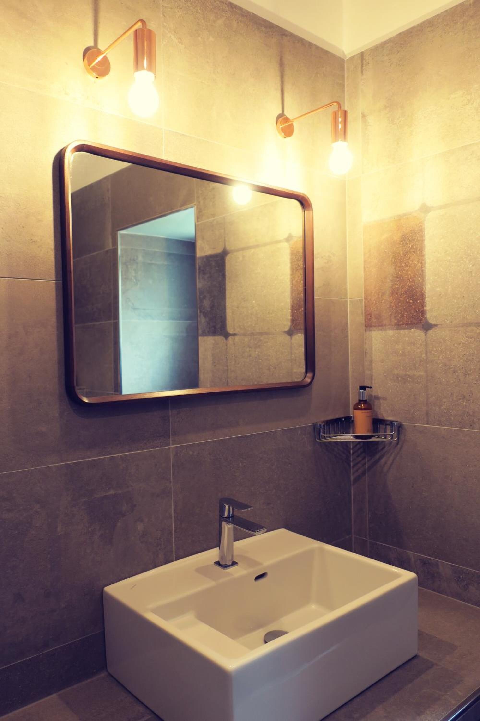 Een moderne badkamer met een rechthoekig wastafelmeubel, een spiegel bevestigd aan de muur en twee wandlampen.
