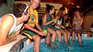 Un grupo de personas sentadas junto a una piscina, algunas sosteniendo bebidas.
