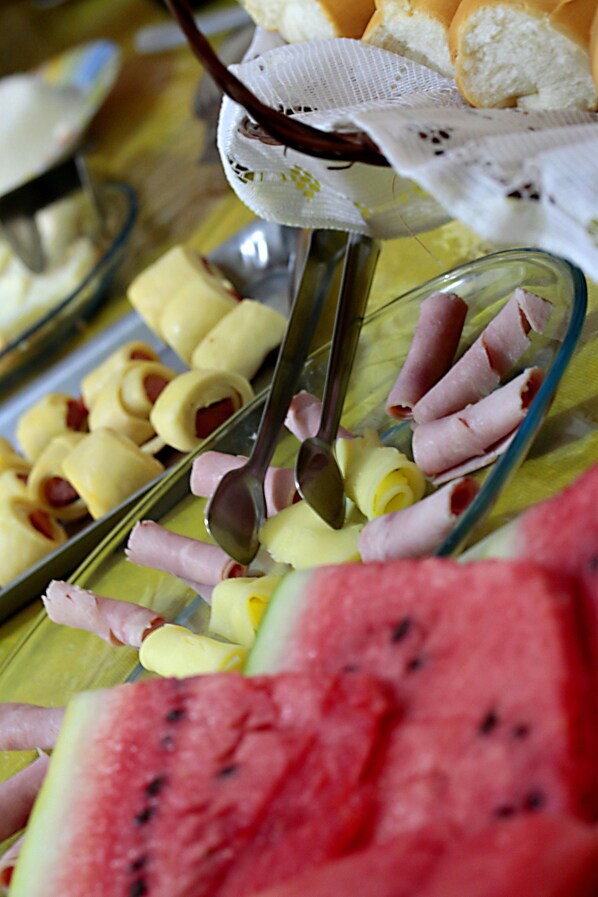 A buffet with various food items including watermelon slices, cheese, and meat rolls. - Pousada Papagaio - Hostel (Cairu)