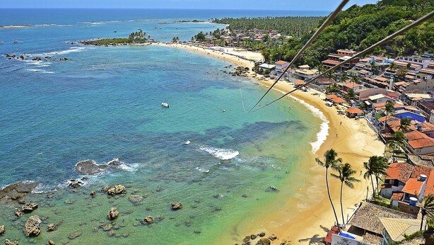 Un pueblo costero con playa, aguas cristalinas y una combinación de edificios residenciales y comerciales.