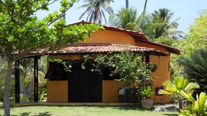 Un petit bâtiment jaune, surmonté d’un toit en tuiles, entouré d’une végétation luxuriante et de palmiers.