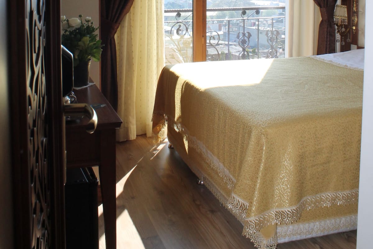 A bedroom with a large bed, a view of the city, and a balcony with a railing.